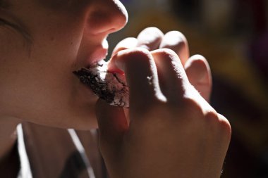 Çocuk, dişleriyle şeker serpiştirilmiş bir parça çikolatalı kurabiyeyi ısırıyor.