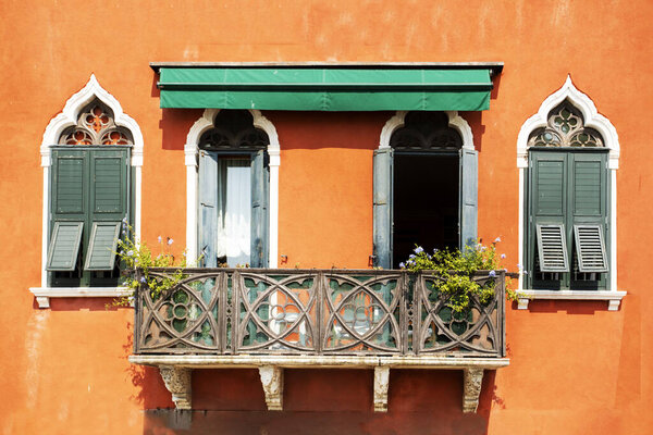 Beautiful old windows with a balcony with fresh flowers on a building in Venice