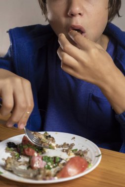 Çocuk karabuğday lapası, sebze salatası ve çatallı et yiyor.