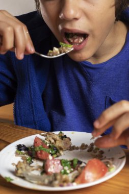 Çocuk karabuğday lapası, sebze salatası ve çatallı et yiyor.