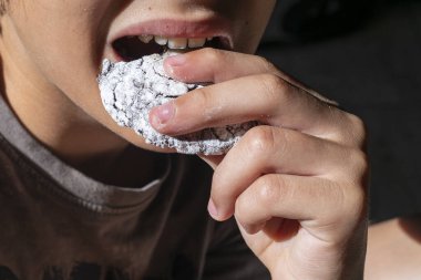 Çocuk, dişleriyle şeker serpiştirilmiş bir parça çikolatalı kurabiyeyi ısırıyor.