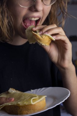 Elinde peynirli sandviçle beyaz bir tabak tut ve ye.