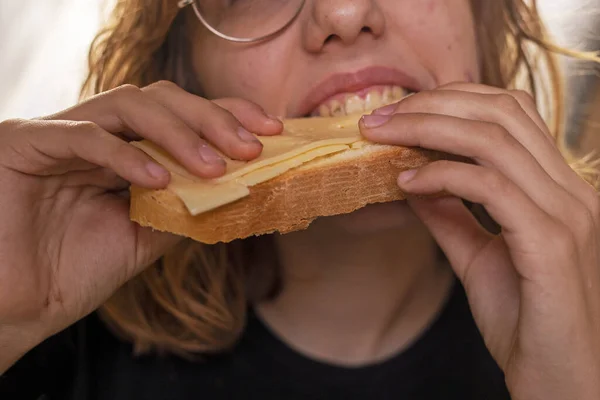 happy teenage girl bites bread with cheese holding with two hands
