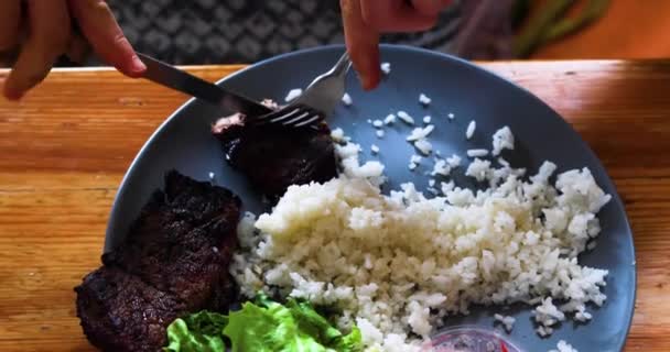 白米の皿にナイフとフォークで焼き肉を切った フラットレイ — ストック動画