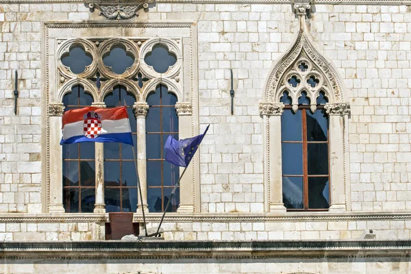 ancient windows with and sculptures in an ancient building with the flag of Croatia and NATO of Roman masonry