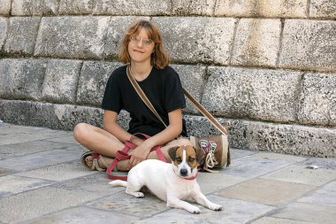 Gözlüklü mutlu kız güneşli bir günde Jack Russell Terrier köpeğiyle oturur.