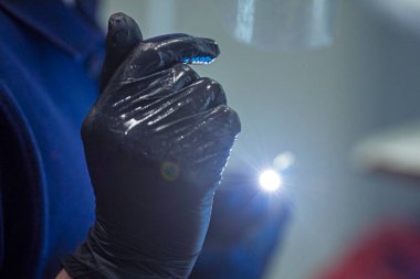 Diş hekimi dişlerini tedavi ederken makinenin başlığını tek kullanımlık eldivenlerin içinde bir el feneriyle tutuyor. Diş bakımı ve bakımı