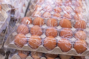 Çiftlik tavuğu kahverengi yumurtaları plastik filmle tezgahın üstünde.