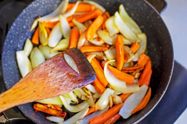 Tahta bir spatula kullanmak, kızartma tavasında soğan ve havuç parçaları karıştırmak, sebzelerle karıştırmak. Sağlıklı beslenme