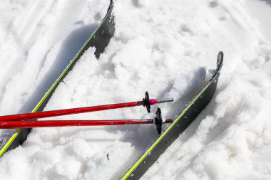Güneşli bir günde karlı bir yamaçta kayak direkleri ve kayaklar
