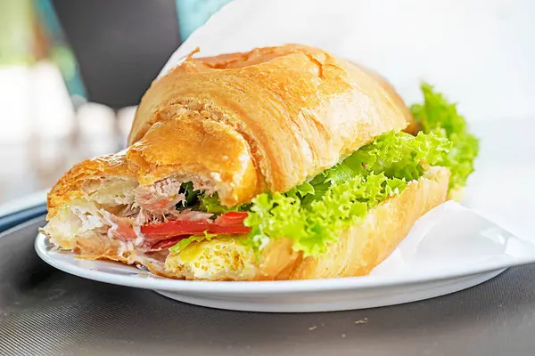 stock image biting into a croissant with vegetables and tuna on a table in a cafe outside. Snack