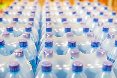 Süpermarketteki raflarda mavi kapaklı plastik kaplarda paketlenmiş karbonatlı içme suyu.