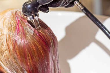 Kuaför boyamadan sonra parlak pembe uzun saç tellerini yıkar.