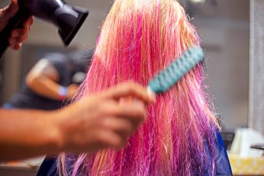 Kuaför, saç kurutma makinesi ve tarak ile boyadıktan sonra parlak pembe ve mor iplikçikler üzerinde stil yaratıyor. şık saç stilleri
