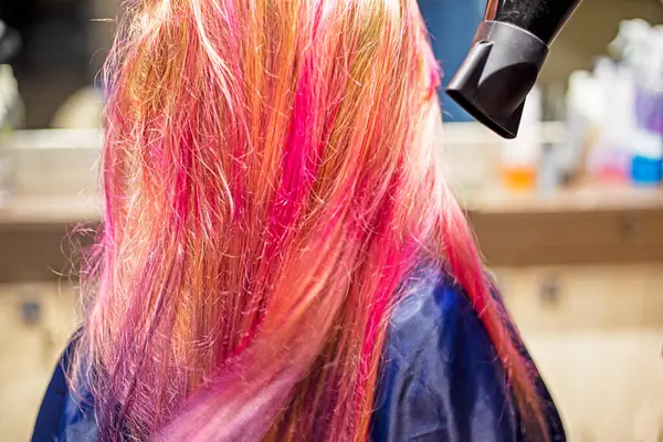 stock image stylist creates styling on bright pink and purple strands of a blonde after dyeing with a hairdryer and comb. stylish hairstyles