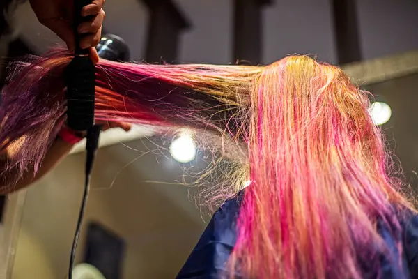 stock image stylist creates styling on bright pink and purple strands of a blonde after dyeing with a hairdryer and comb. stylish hairstyles