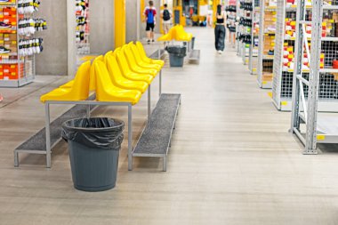 Süpermarketteki çöp kutusunun yanındaki ayakkabı reyonunda ayakkabı giymek için sarı şık koltuklar.