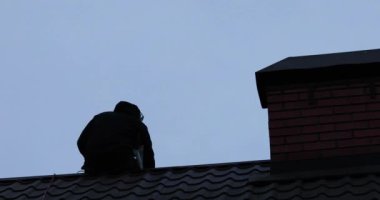 Çatıda oturan işçiler bulutlu havada güneş panelleri kurarken çatıya bir ip fırlatıyorlar.