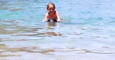 Mutlu kız, denizde babasının sırtına tutunarak yüzmeyi öğreniyor. Okul tatili. Denizde tatil.