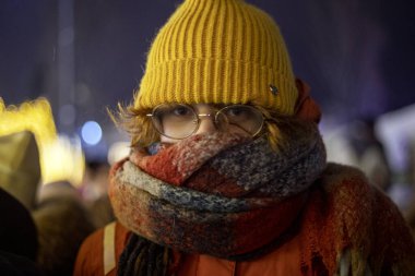 Sarı şapkalı mutlu genç kız bir Noel şehrinin arka planında eşarba sarılmış.