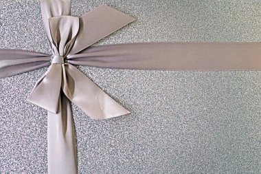Gümüş renkli bir arkaplan, bağlı bir kurdele ve hediye olarak bir fiyonk. Hediyeler ve sürprizler