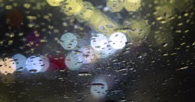 Yağmurda karanlıkta trafikte damlaların ve ışıkların bulanık arkaplanı. Yollarda güvenlik ve dikkatlilik, kötü görüş.