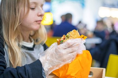 Liseli kız teneffüslerde eldiven içinde çizburger yer. Okul yemeği