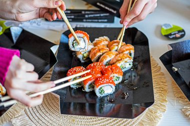  Aile, yemek çubuklarıyla hazırlanmış suşi ruloları yer. Japon tarzında şenlikli bir akşam.