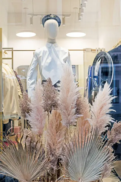 Süpermarketin vitrininde kurumuş otlar ve çiçeklerle çevrili bereli bir manken. Eko tasarımı