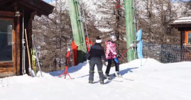 Genç bir kız Alplerdeki bir İtalyan kayak merkezinde T-bar asansörüyle yokuşa tırmanıyor..