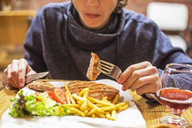 Çocuk domuz pirzolası, patates kızartması ve ketçap yiyor.