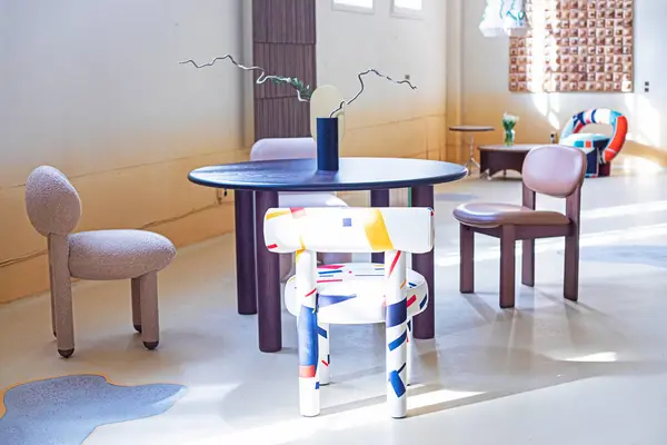 İç taraftaki yuvarlak bir masanın yanında farklı şekillerde modern sandalyeler.