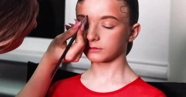 Usta, bir fırçayla makyaj yapıyor. Lise birdeki dans turnuvasında ifade yeteneği için bir kızın kaşlarını boyuyor.