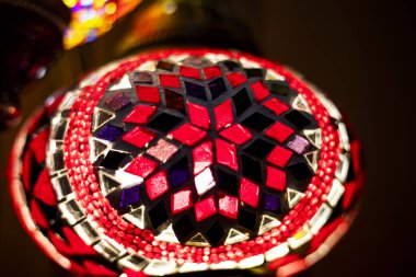 Kırmızı gölgeli geometrik desenli koyu bir zemin üzerinde boyalı cam lamba.