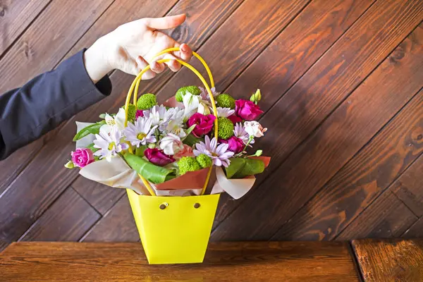 Tahta arka planda bir buket çiçekli sarı bir sepet tutuyordu. Kutlarım. Kadınlar Günü, Anneler Günü