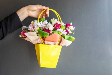 Gri arka planda çiçeklerle dolu bir çiçek sepeti tutuyordu. Kutlarım. Kadınlar Günü, Anneler Günü