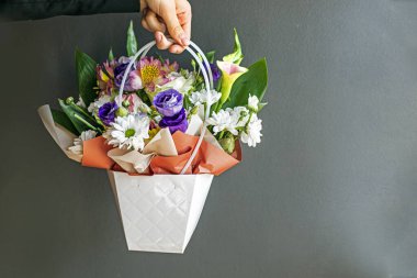 Gri arka planda çiçeklerle dolu bir çiçek sepeti tutuyordu. Kutlarım. Kadınlar Günü, Anneler Günü