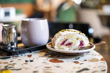 piece of meringue roll with pistachio and raspberry cream with a cup of ginger in a cafe