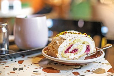 piece of delicious meringue roll with pistachio and raspberry cream with a cup of ginger in a cafe