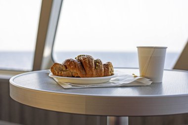 Bir yolcu gemisinde tek kullanımlık fincanda kahveli kruvasan. Sabah atıştırması