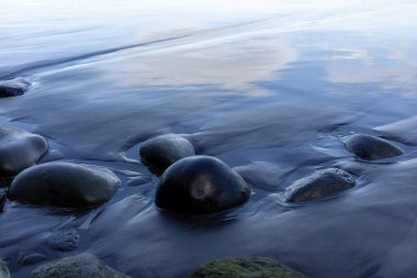 Siyah ıslak kumsalda yansımalı yuvarlak taşlar. Yüksek kalite fotoğraf