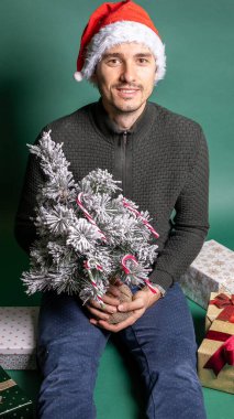 Kırmızı şapkalı adam yeşil arka planda bir sürü hediye paketlemiş.