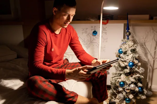 Młody Mężczyzna Świątecznej Piżamie Ogląda Łóżku Tablet Wysokiej Jakości Zdjęcie — Zdjęcie stockowe