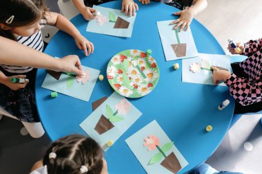 Kreşteki çocuklar yuvarlak bir masada oplekasyon ve çizimler yaparlar..