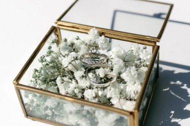 Nişan yüzükleri çiçeklerle süslenmiş şeffaf bir kutuda..