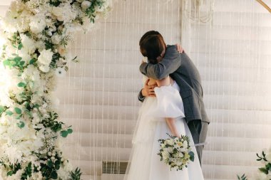 Düğün çifti, tören kemerinin arka planına sarılıyor..