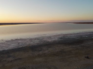 Fotoğraf, tuzlu bir göl üzerinde soluk kesici bir gün batımı yakalıyor, gökyüzünü turuncu ve pembe renklerle dolduruyor. Gölün durgun suları gökyüzünün renklerini yansıtır. Odessa, Ukrayna. 