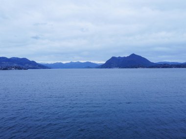 Panoramik deniz manzarası. Sakin deniz, tekneler, tepeli yeşil adalar ve ufukta soluk mavi dağlar, berrak gökyüzü. İtalya, Como Gölü. Yüksek kalite fotoğraf