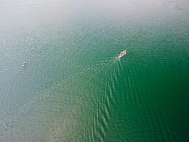 Mavi denizde yüzen beyaz sürat teknesinin hava görüntüsü. Yüksek hızda giden bir teknenin insansız hava aracı görüntüsü. Mavi suda hareket eden bir teknenin üst görüntüsü. Su taşımacılığı ve yaz mevsimi. Yüksek kalite fotoğraf