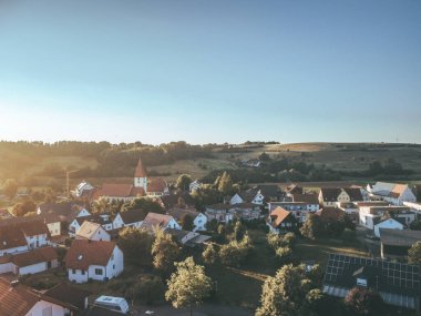 Bu stok fotoğrafı tarlalar ve tepelerle çevrili küçük bir kasabayı gösteriyor. Evlerin çoğu beyaz ve kırmızı çatıları var. Fotoğrafın açık ve güneşli bir gökyüzü var. Alman köyü insansız hava aracı çekimi..